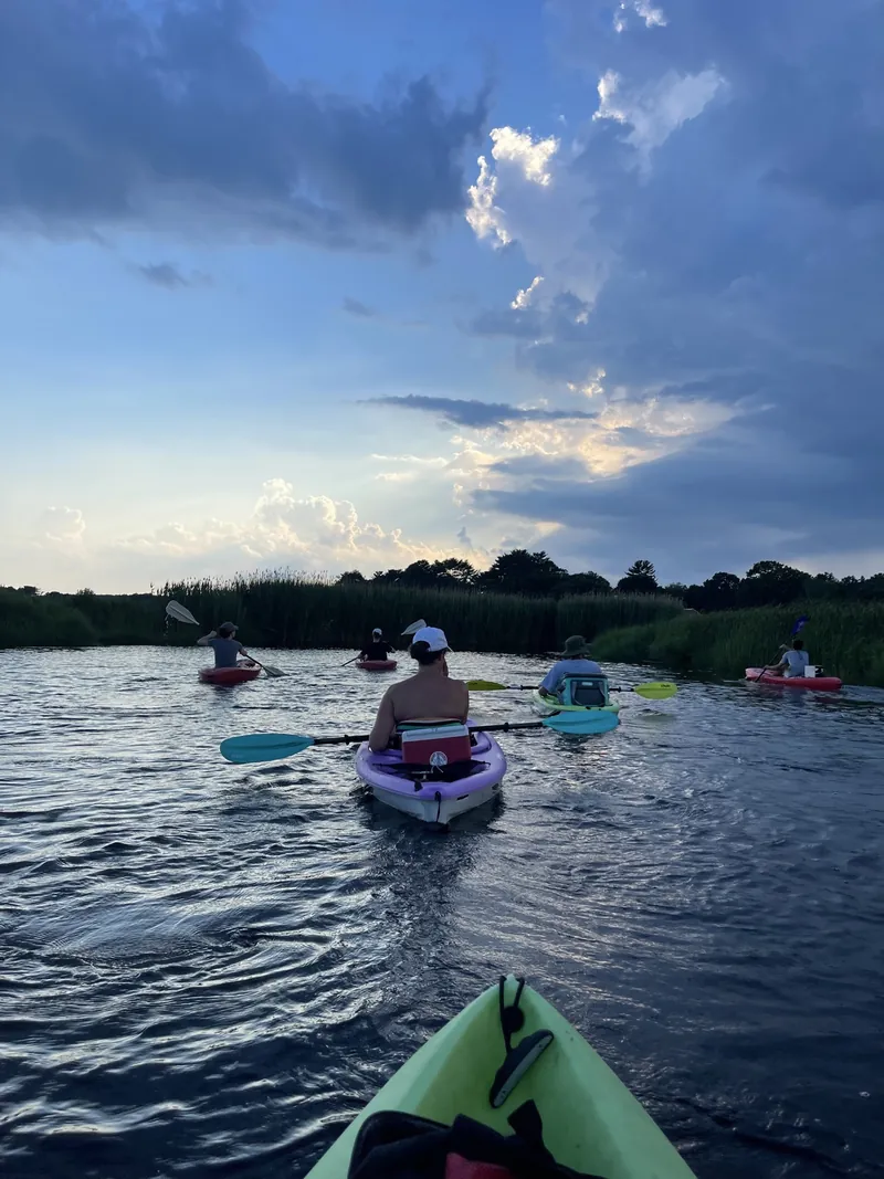 Kayakers paddling the South River salt marsh in Marshfield, MA at dusk